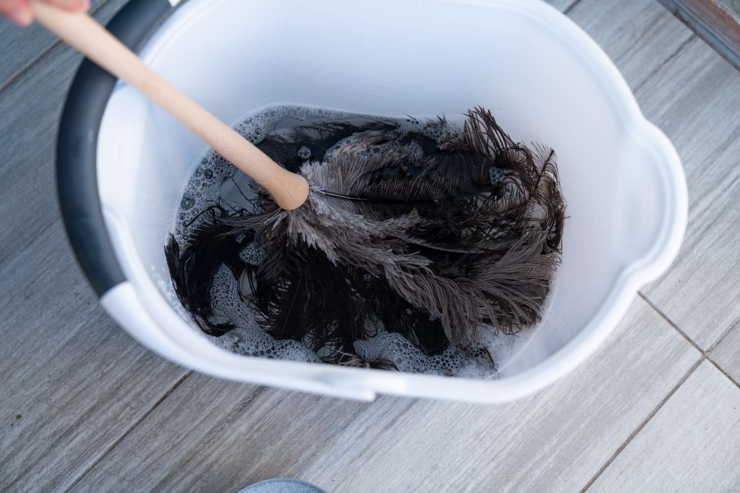 Feather duster cleaned in a bucket filled with a cleaning solution.