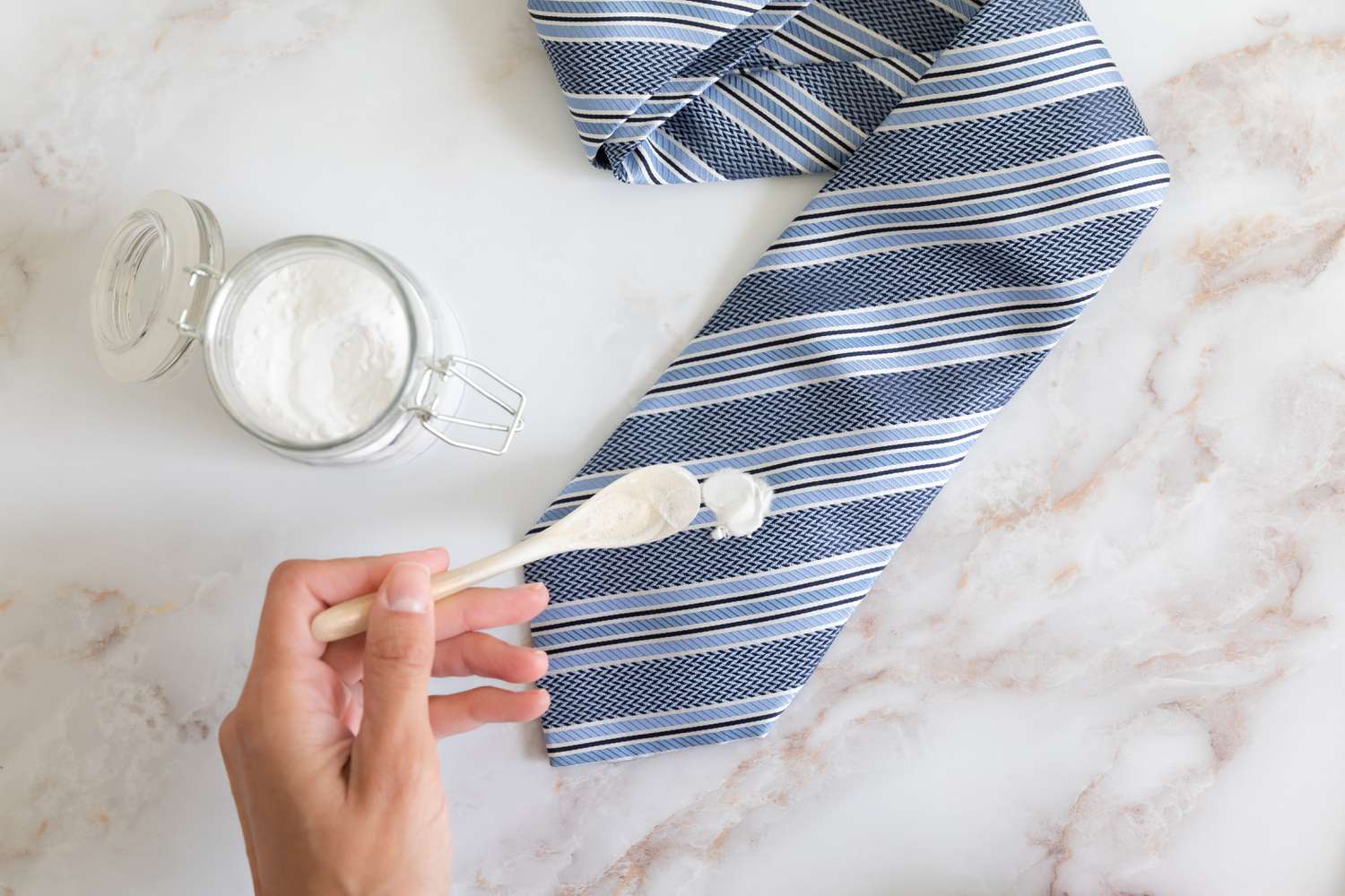 A spoonful of baking soda sprinkled onto a sticky substance on a blue striped necktie.