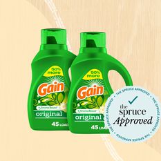 A composition featuring two bottles of Gain Laundry Detergent Liquid Soap with Aroma Boost set against a soft tan backdrop.