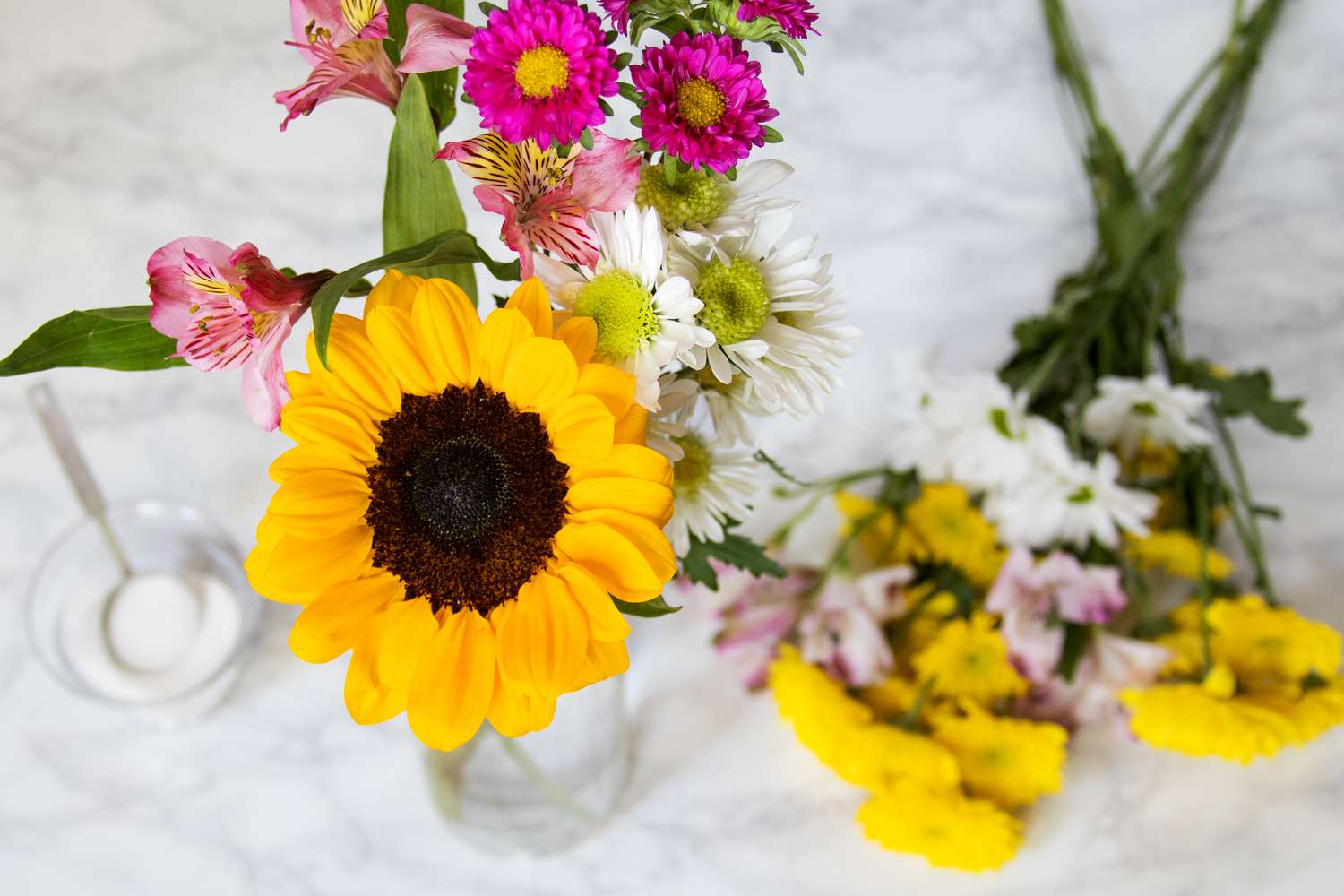 Freshly cut sunflowers, daisies, and lilies arranged in a vase filled with a sugar-water solution.